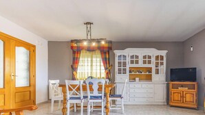 A dining area with a wooden table and chairs, a white cabinet with glass doors, a television on a wooden stand, and a colorful curtain. - Family Oasis in Comarruga: Pool and Relaxation (El Vendrell)