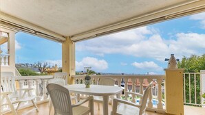 A covered outdoor area with a table and chairs, a view of the city, and a balcony railing. - Family Oasis in Comarruga: Pool and Relaxation (El Vendrell)