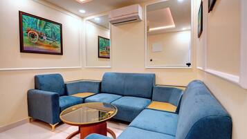 Una habitación con un sofá seccional azul, una mesa de centro de vidrio y dos cuadros en la pared.