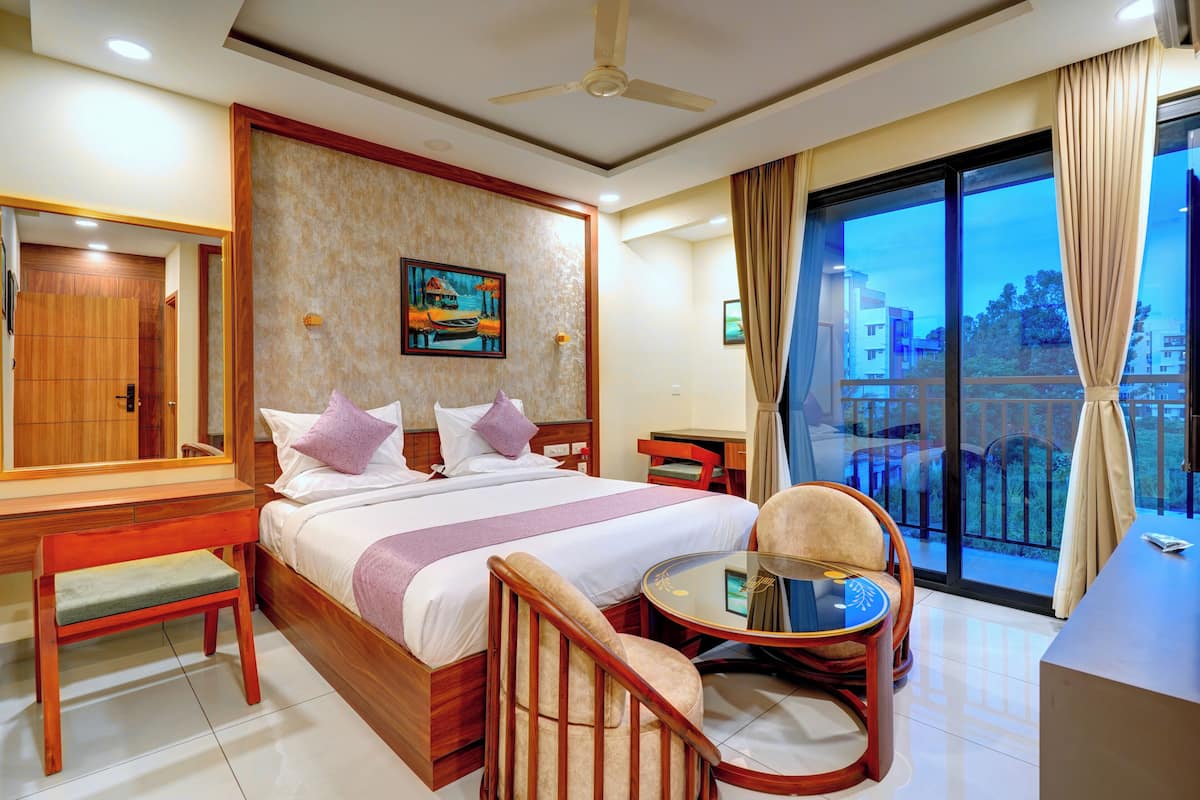Habitación de hotel con cama, escritorio, silla, mesita y balcón con vistas.