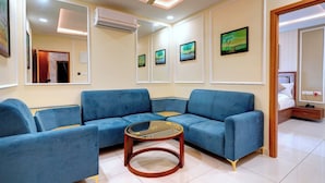A modern living room with a blue sofa set, a glass coffee table, and wall-mounted air conditioning units.