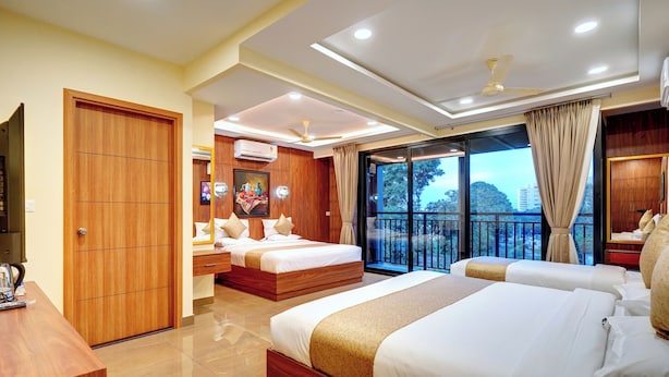 A hotel room with two beds, a desk, a ceiling fan, and a large window with a view.