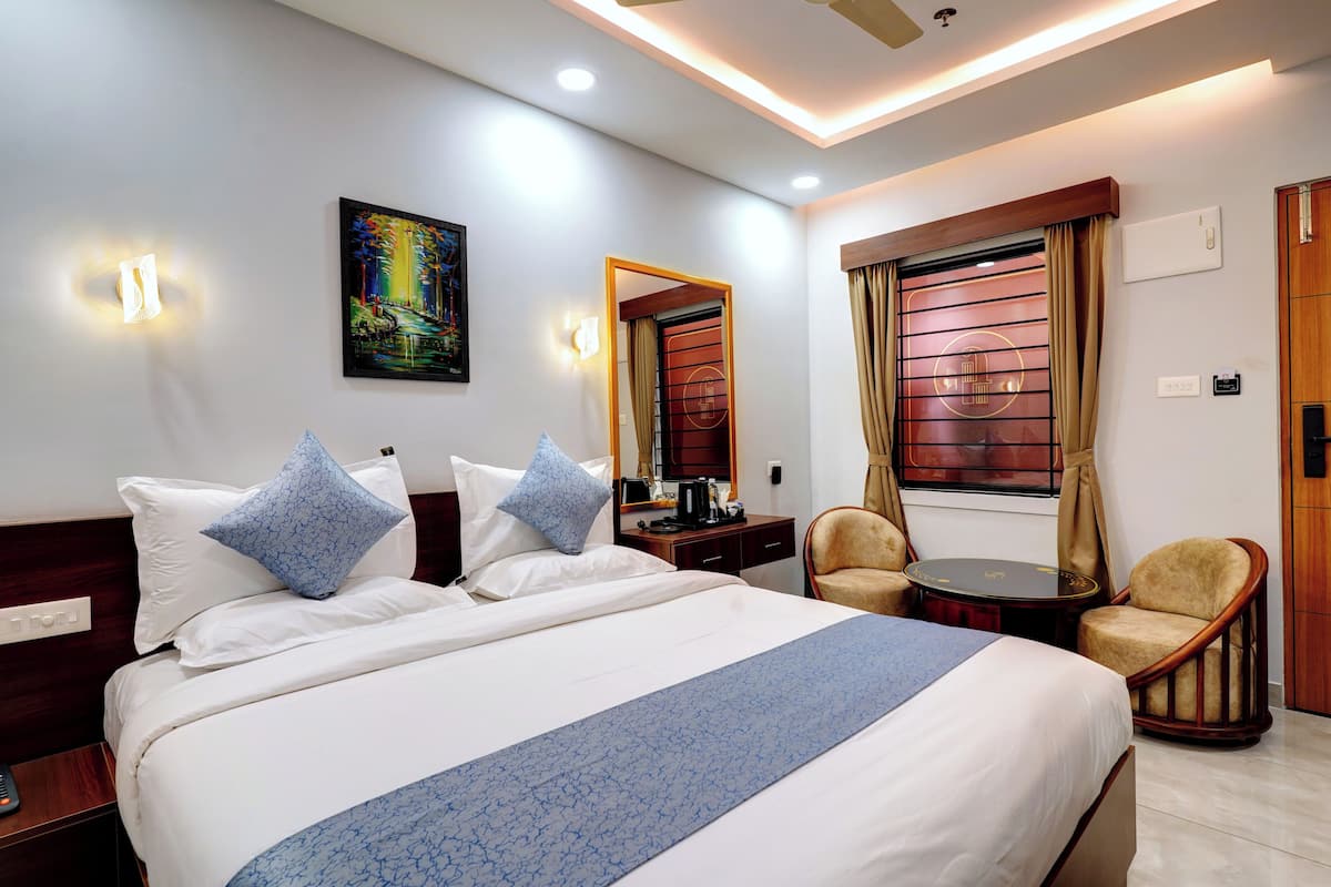 Habitación de hotel con una cama grande, dos sillas, una mesita, un cuadro en la pared y una ventana con cortinas.