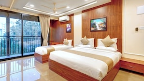 A hotel room with a large bed, a ceiling fan, an air conditioning unit, a window with a view, and a painting on the wall.