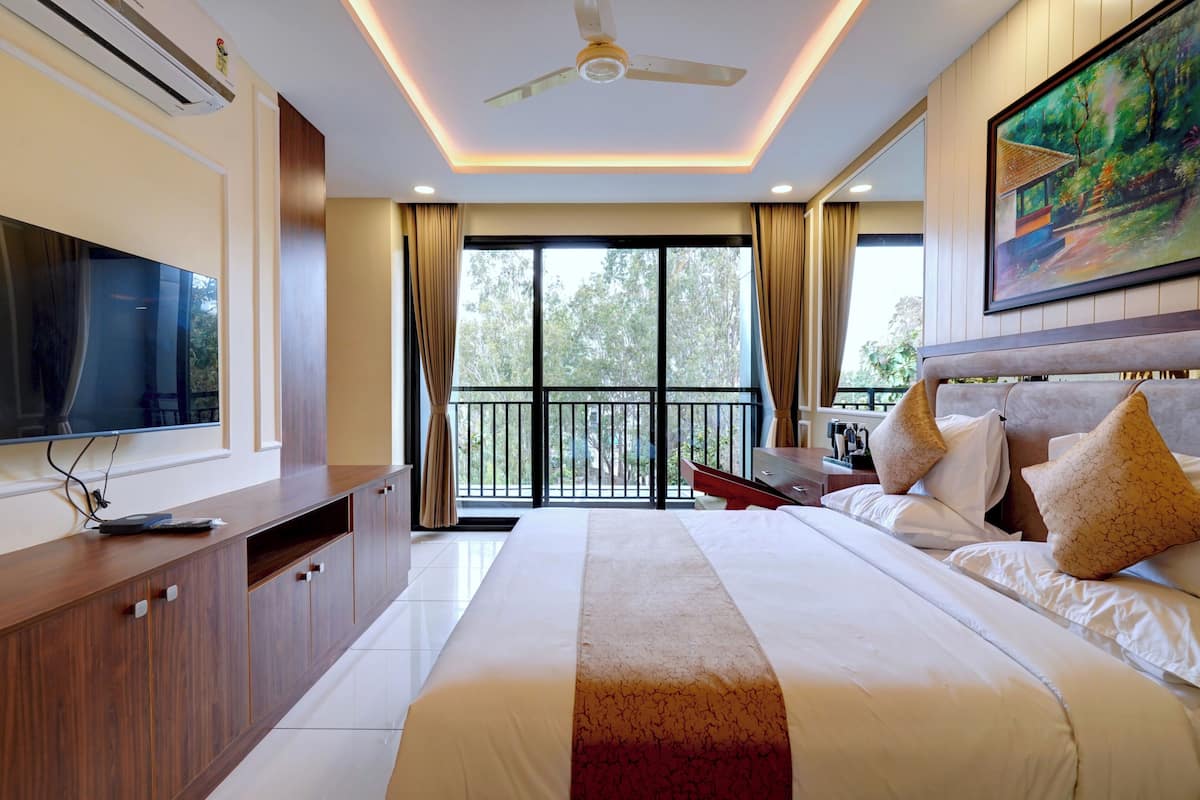 Habitación de hotel con cama, televisor, aparador de madera, ventilador de techo y balcón con vista a árboles.