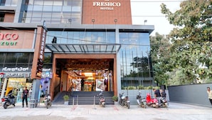 A modern building with a sign for Freshco Hotels, a visible entrance, and several parked scooters.