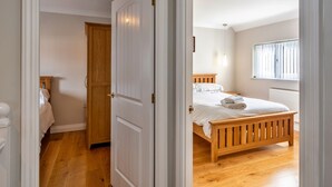 A bedroom with a wooden bed, a nightstand, a window with blinds, and a door leading to another room.