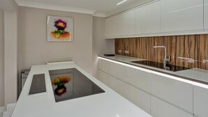 A modern kitchen with a central island, white cabinetry, a wooden accent wall, and a painting on the wall.