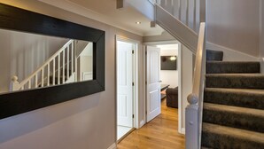 A staircase with a dark carpet and white balusters, a hallway with wooden flooring, and a large mirror on the wall.
