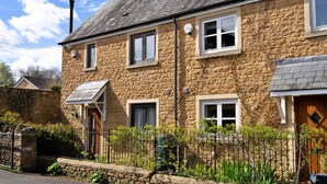A stone house with a sloped roof, multiple windows, a wooden door, and a stone wall. - Hollies Cottage, Oak (3 bed) (Bower Hinton)
