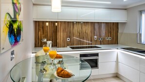 A modern kitchen with a glass table, white cabinets, and a wooden accent wall. - Hollies Cottage, Oak (3 bed) (Bower Hinton)