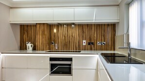 A modern kitchen with white cabinetry, a built-in oven, and a wooden accent wall. - Hollies Cottage, Oak (3 bed) (Bower Hinton)