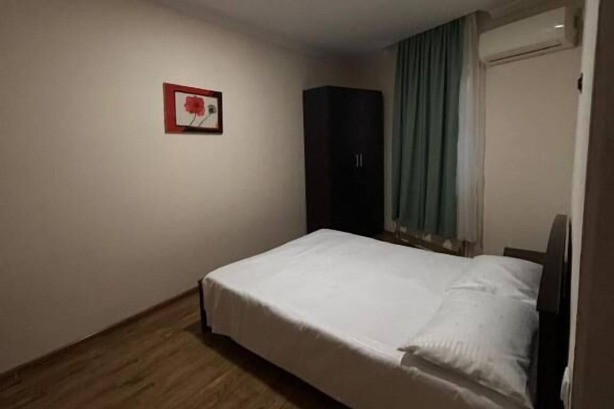 A room with a bed, a wardrobe, a picture on the wall, and a window with curtains.