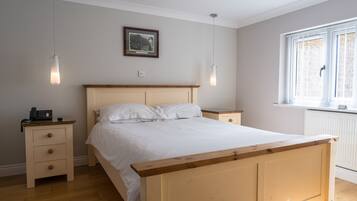 A bedroom with a wooden bed, bedside tables, a nightstand with a phone, a framed picture on the wall, and a window with blinds.