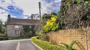 Une maison en pierre avec un toit en tuiles, une route pavée et un mur de pierre orné de verdure.