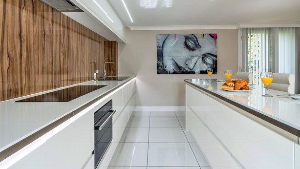 Une cuisine moderne avec un mur d’accent en bois, un grand tableau et un coin petit-déjeuner avec des croissants et du jus d’orange.