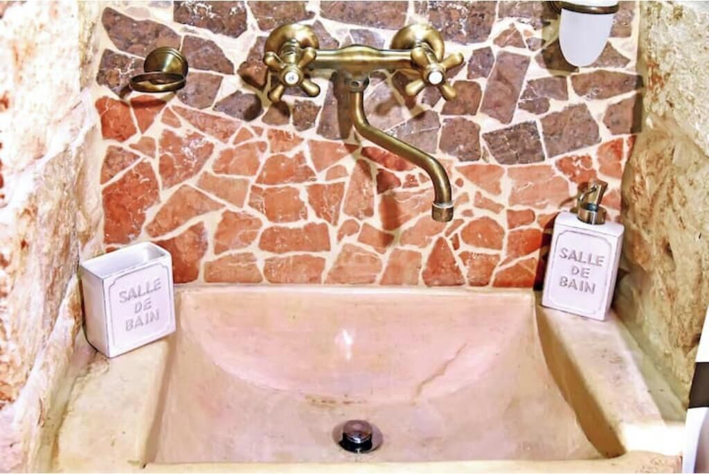 Um banheiro com parede em mosaico de pedra, uma torneira de latão e duas placas com a inscrição 'SALLE DE BAIN'.