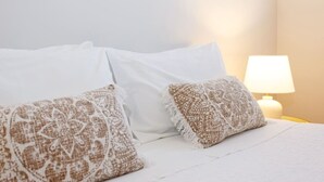 A bed with white bedding and two patterned pillows, a bedside lamp, and a plain wall.