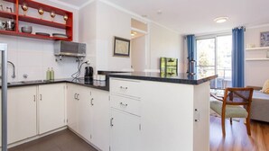 A compact kitchen with white cabinets, a black countertop, and a red shelf.