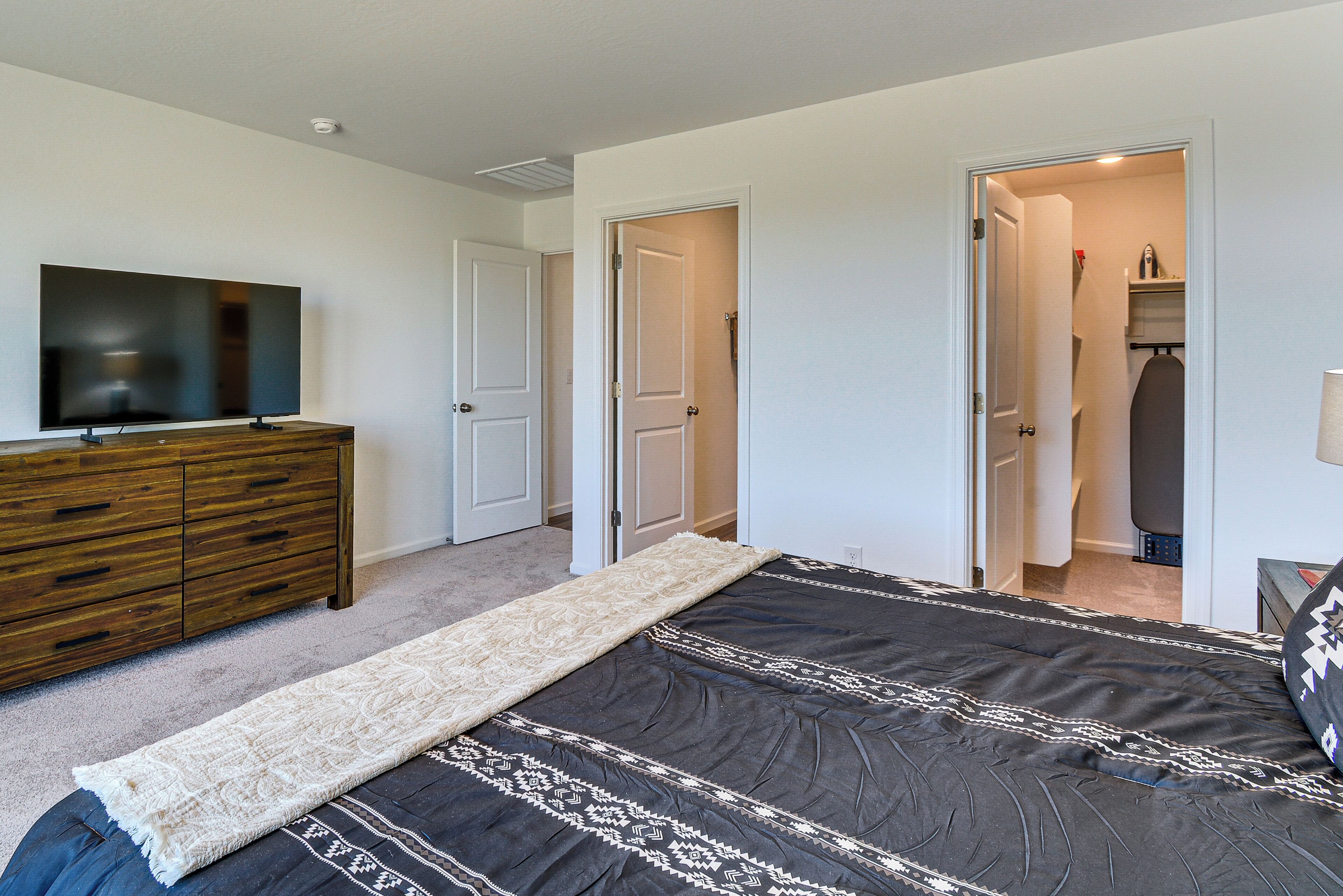 A bedroom with a bed, a dresser, a television, and a door leading to a bathroom.