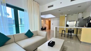 Quarto de hotel moderno com sofá, mesa de centro, área de cozinha e vista pela janela.