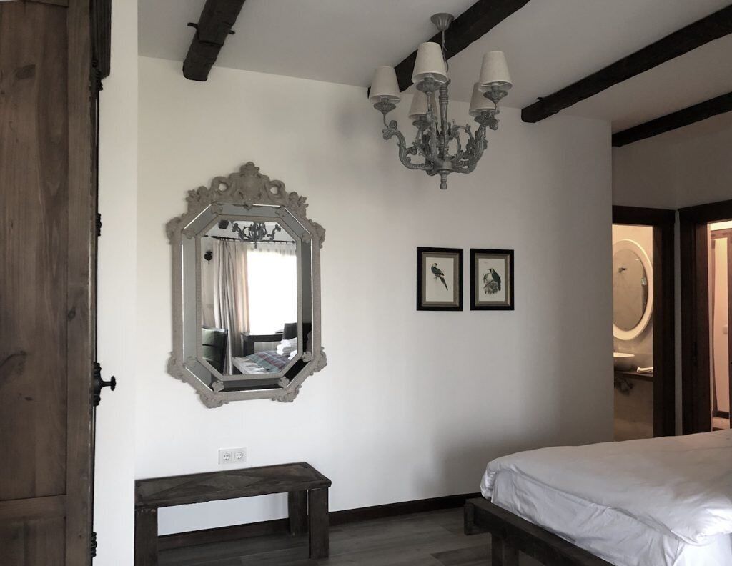 Een slaapkamer met een grote, versierde spiegel, een kroonluchter en twee ingelijste foto's aan de muur.