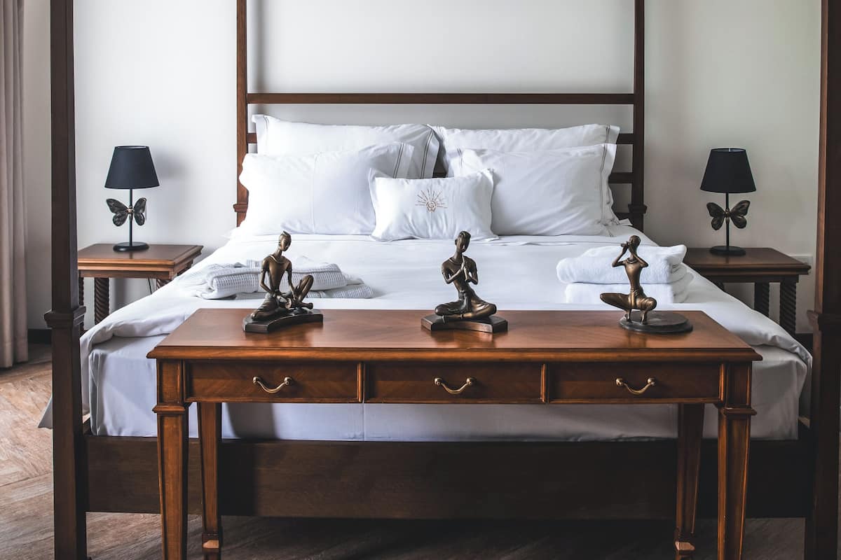 Una cama con dosel de madera, ropa de cama blanca y esculturas decorativas sobre las mesitas de noche.