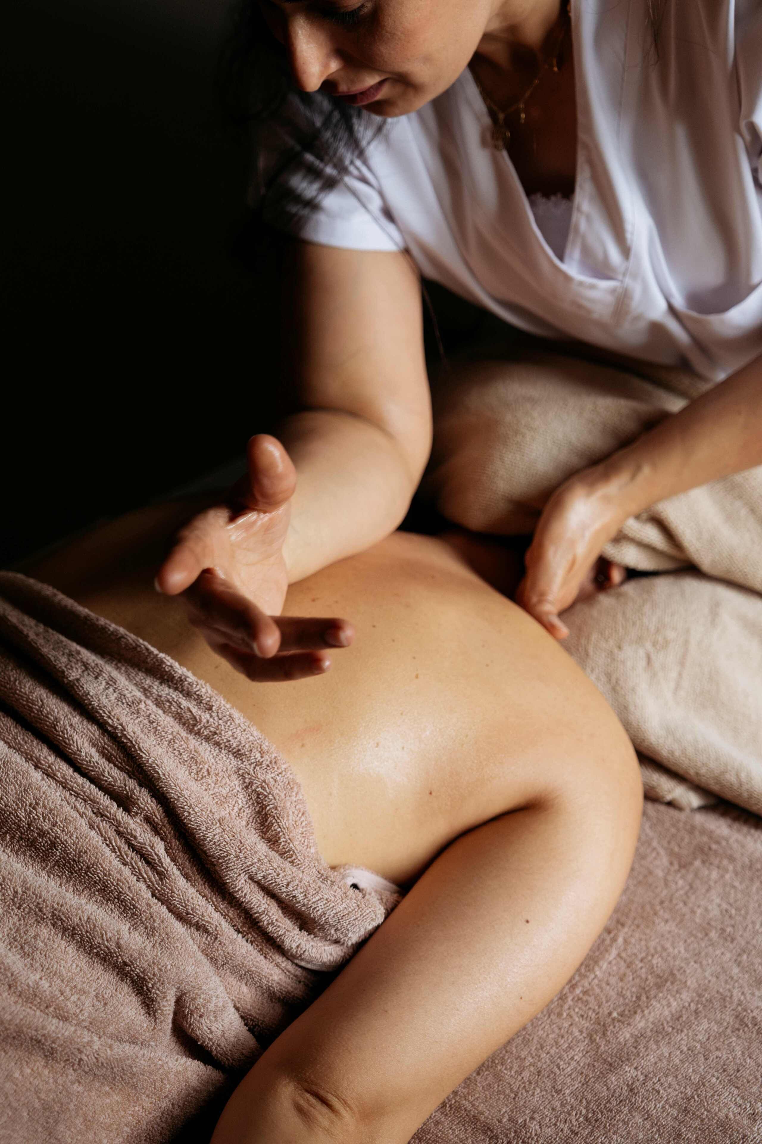 A person receiving a massage on a bed with a brown blanket.