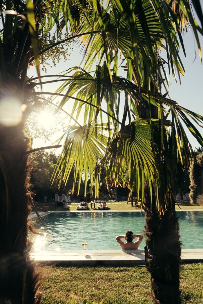 Piscina rodeada de palmeras y una persona relajándose junto a ella.