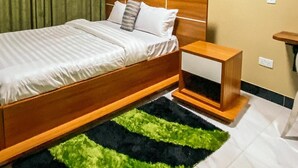 A bedroom with a bed, a nightstand, a rug, and a curtain. - WYNE'S MINI SUITE (Mbale)