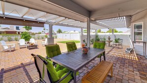 Uma área de varanda coberta com mesa e cadeiras, um ventilador de teto e vista para o quintal.