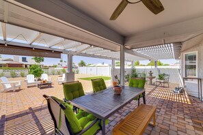 Ein überdachter Patio-Bereich mit Tisch und Stühlen, einem Deckenventilator und Blick auf den Garten.
