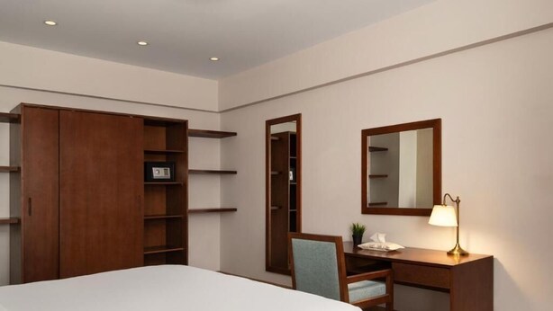 A hotel room with a bed, a desk with a lamp, a chair, a wardrobe, and a mirror. - ICONIA Zamalek (Zamalek)