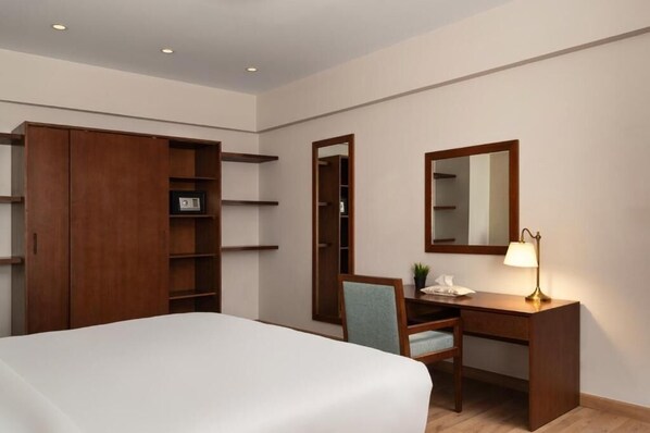 A hotel room with a bed, a desk with a lamp, a chair, a wardrobe, and a mirror. - ICONIA Zamalek (Zamalek)