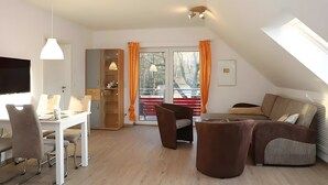 En moderne stue med spiseplads, sofa, tv og et stort vindue med gardiner.