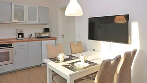 Et moderne køkken med spiseplads, inklusiv et bord med stole, en kaffemaskine og et fladskærms-tv monteret på væggen.
