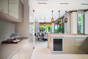 Eine moderne Küche mit integriertem Kühlschrank, einer Essecke mit Tisch und Stühlen sowie großen Fenstern mit Blick auf Grünflächen.