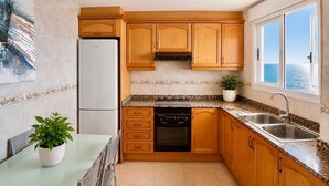 A kitchen with wooden cabinets, a refrigerator, an oven, a sink, and a window with a view.