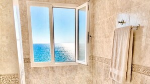 A bathroom with a bathtub, two toilets, a bidet, and a large window with a view of the sea.