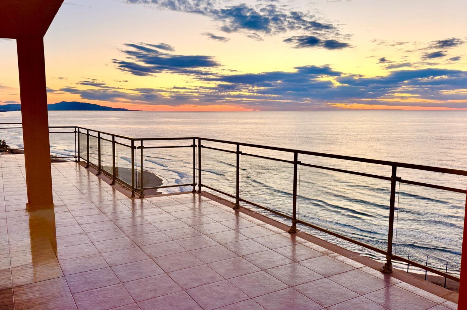 A balcony with a railing overlooking a calm sea during sunset.