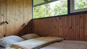 A room with wooden panel walls, a bed with a mattress and pillows, and two wall-mounted lamps.