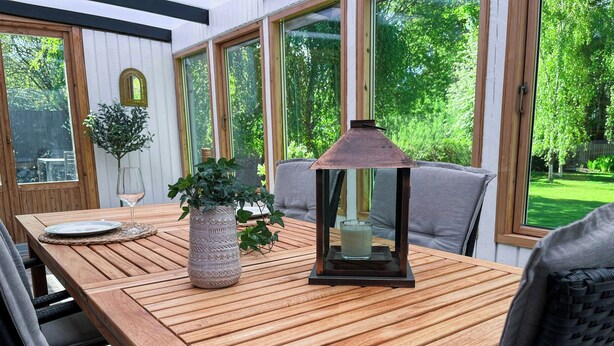 A wooden table with a glass and a potted plant, surrounded by chairs and large windows.