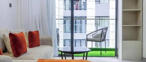 A modern living room with a sofa, a round table, and a view of a balcony with a chair.