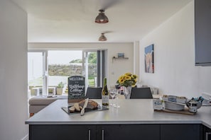 A modern kitchen with a central island, a chalkboard sign, and a view of the outside. - Buttercup Cottage (Wadebridge)
