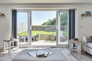 A modern living room with a large sliding glass door leading to a garden. - Buttercup Cottage (Wadebridge)