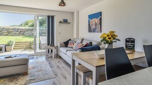 Una sala de estar moderna con un sofá, una mesa de comedor y vista a un jardín a través de un ventanal.