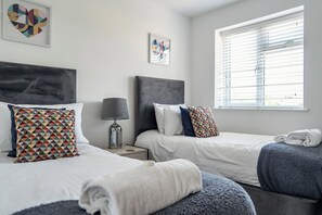 A hotel room with two beds, a nightstand with a lamp, and artwork on the walls. - Buttercup Cottage (Wadebridge)