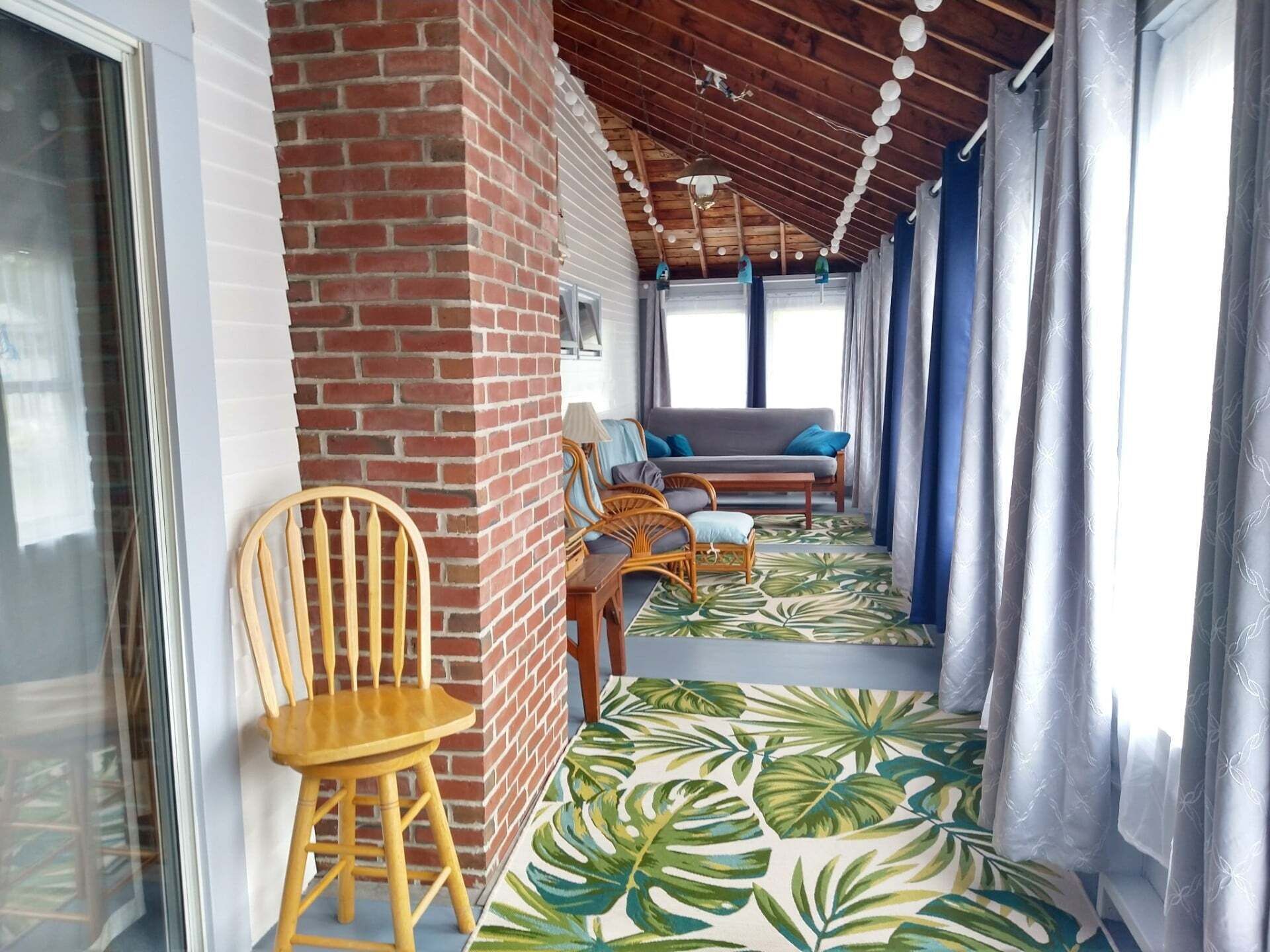 Un porche cubierto con un muro de ladrillo, una silla de madera, un sofá y un suelo con diseño.