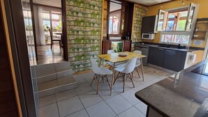 A kitchen with a dining area, a microwave, and a window. - Maison aux Portes du Sud Sauvage – Family Home with Pool & Hot Tub (Saint Joseph)