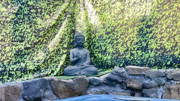 A hot tub with a Buddha statue, surrounded by a rock wall and foliage. - Maison aux Portes du Sud Sauvage – Family Home with Pool & Hot Tub (Saint Joseph)